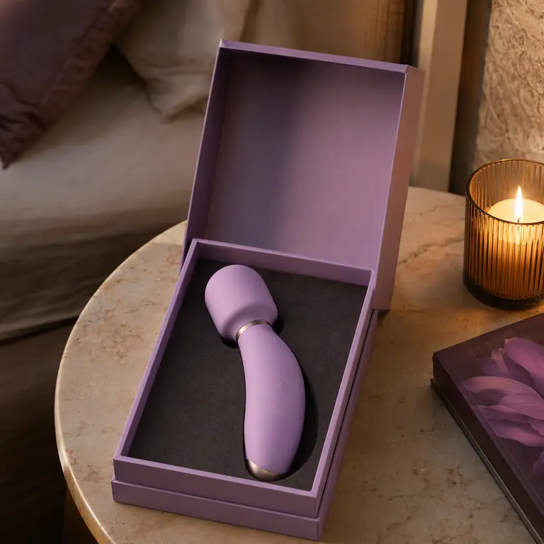 Lifestyle shot: a personal massager in its gift box on a bedside table (fictional brand “Lunefield”)